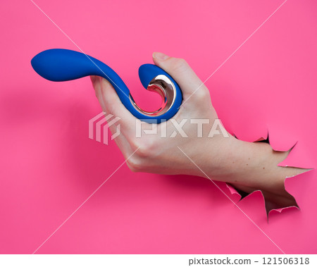 Hand with blue vibrator sticking out through pink paper background.  121506318