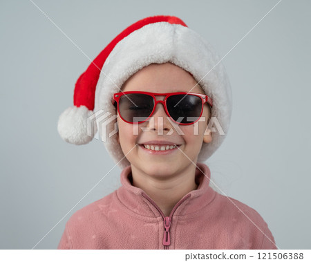 Portrait of a cute Caucasian girl wearing a Santa Claus hat and sunglasses on a white background.  121506388
