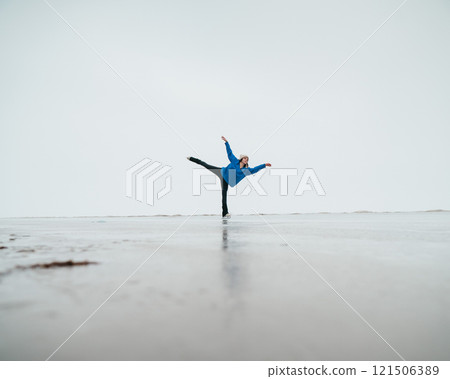 Caucasian woman in a blue sweater is skating on a frozen lake. Figure skater performs a swallow.  121506389