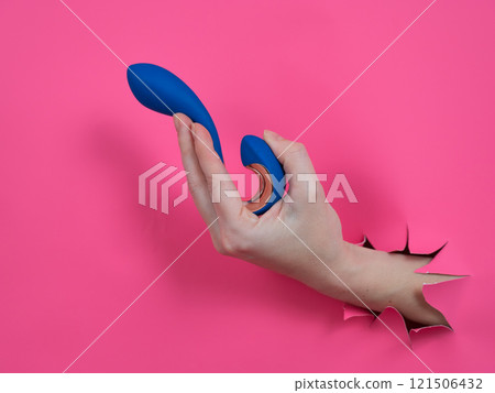 Hand with blue vibrator sticking out through pink paper background.  121506432