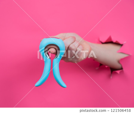 Female hand sticking out of pink paper background with blue curved vibrator sex toy.  121506458