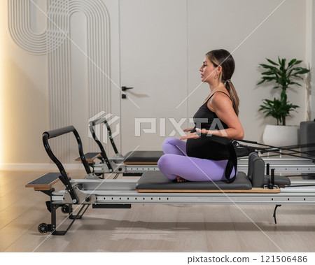 Pregnant woman doing Pilates exercises on a reformer machine. Pregnant woman doing Pilates exercises on a reformer machine. 121506486