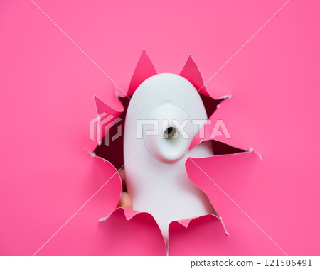 White vacuum clitoral vibrator sticking out through pink paper background. Sex toy.  121506491