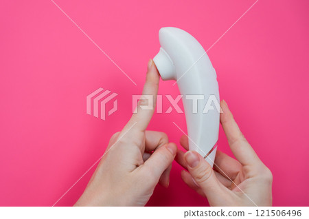 Woman holding white vacuum clitoral vibrator on pink background.  121506496