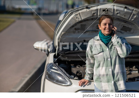 Caucasian woman laughing and calling on phone asking for help standing near car with open hood. Caucasian woman laughing and calling on phone asking for help standing near car with open hood. 121506521