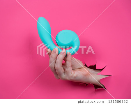Hand with blue vibrator sticking out through pink paper background. Copy space.  121506532