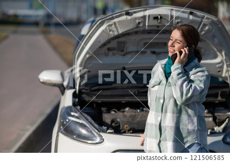 Caucasian woman laughing and calling on phone asking for help standing near car with open hood. Caucasian woman laughing and calling on phone asking for help standing near car with open hood. 121506585