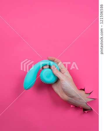 Hand with blue vibrator sticking out through pink paper background. Vertical photo. Hand with blue vibrator sticking out through pink paper background. Vertical photo. 121506586