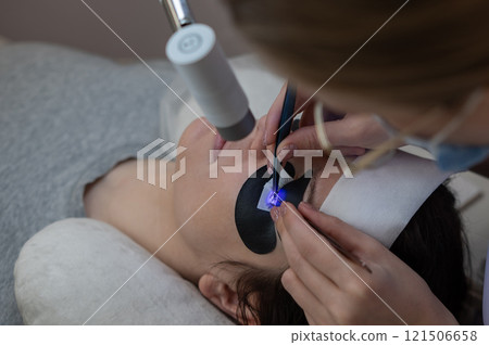 A woman undergoing eyelash extension procedure using an ultraviolet lamp. A woman undergoing eyelash extension procedure using an ultraviolet lamp. 121506658