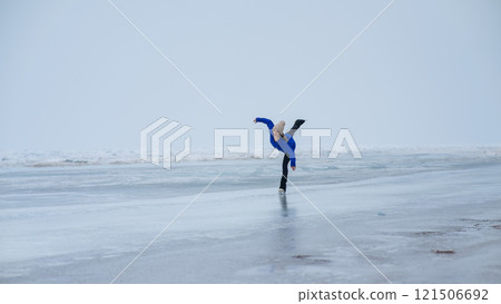 Caucasian woman in a blue sweater is skating on a frozen lake. Figure skater performs a swallow.  121506692