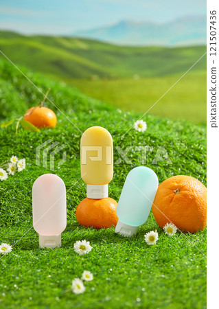 The promotional photo for sunscreen product was shot on green grass hill background. Some cosmetic tube without label displayed in center with fresh fruit and some tiny flowers 121507436