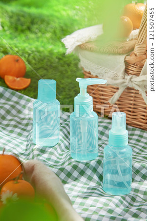 Overhead shot with a frontal view of a blue set product mockup placed on a green picnic mat, next to some tangerines and a basket. A concept for a picnic in the grass, perfect for cosmetics ad photos. 121507455