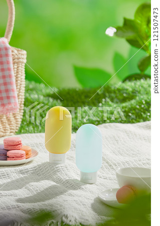A high-angle picture of a picnic theme for sunscreen ads, shows two unbranded bottle mockups placed in the center of a mat, surrounded by a macaroon dish, tea set, and a bag in. Green grass background A high-angle picture of a picnic theme for sunscreen ads, shows two unbranded bottle mockups placed in the center of a mat, surrounded by a macaroon dish, tea set, and a bag in. Green grass background 121507473