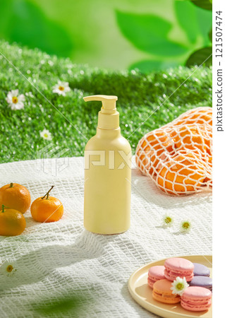 An unlabeled cosmetic bottle is positioned in front, next to a macaroon dish, some oranges, and a few feverfew flowers, the promotional template shot with a picnic setting on a green grass backdrop. An unlabeled cosmetic bottle is positioned in front, next to a macaroon dish, some oranges, and a few feverfew flowers, the promotional template shot with a picnic setting on a green grass backdrop. 121507474