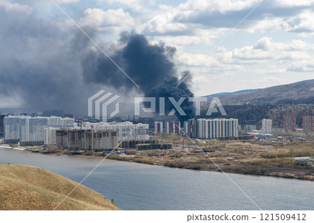Black smoke from a fire in a city on the other side of the river. 121509412
