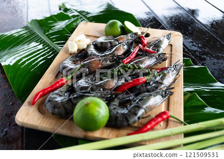 In a lively tropical kitchen, freshly caught tiger prawns are beautifully displayed on banana leaves, accompanied by fragrant herbs and spices. In a lively tropical kitchen, freshly caught tiger prawns are beautifully displayed on banana leaves, accompanied by fragrant herbs and spices. 121509531