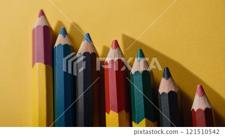 A row of colorful pencils stands on a bright yellow background, highlighting the different colors and tips. These artistic tools are perfect for drawing, coloring, and expressing creativity. 121510542