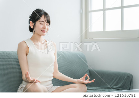 Young Asian woman doing light yoga, meditation, mindfulness, morning activity on the sofa at home (morning routine) Young Asian woman doing light yoga, meditation, mindfulness, morning activity on the sofa at home (morning routine) 121510781