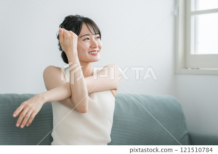 年輕的亞洲女性在家裡的沙發上做輕微的伸展運動和瑜伽（早上的例行活動） 121510784