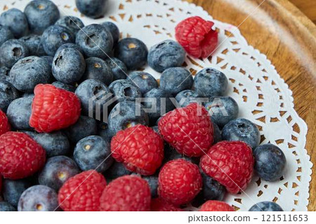 A beautiful display of vibrant berries is arranged artfully on an elegant lace doily 121511653