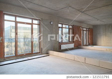 A Modern Unfinished Interior Space Featuring Large Windows Alongside Concrete Walls and Elements 121511791