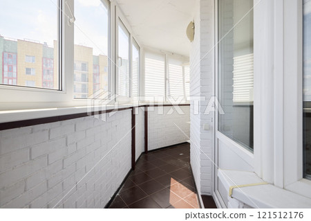 A modern sunlit balcony featuring pristine white walls complemented by warm brown flooring 121512176