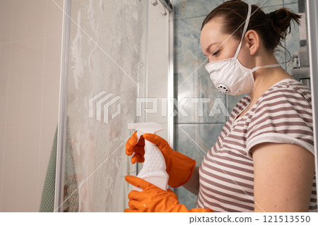 A woman is meticulously cleaning her shower while wearing protective gear for safety A woman is meticulously cleaning her shower while wearing protective gear for safety 121513550