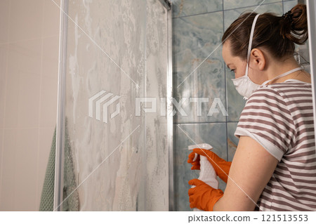A woman is diligently cleaning her shower using a spray bottle filled with cleaner solution A woman is diligently cleaning her shower using a spray bottle filled with cleaner solution 121513553
