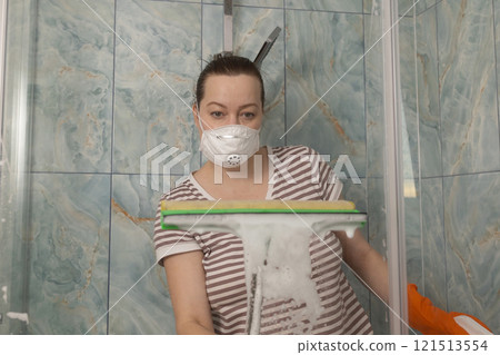 A Woman Diligently Cleaning the Shower with Soap and Wearing a Protective Mask for Hygiene 121513554