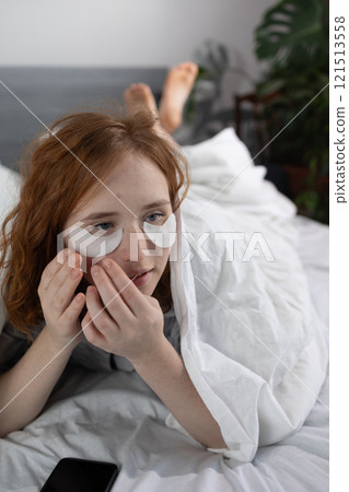 A Woman Applying Eye Patches While Enjoying a Peaceful Relaxing Moment in Her Bed 121513558