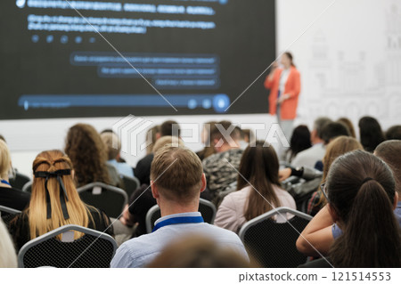 Audience attending a presentation with speaker on stage and displayed content screen 121514553