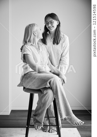 Cute family moment of mom and daughter hugging. Portrait of teenage girl showing her love to mother. Two female in casual clothes smiling and hugging at home. Black and white image. Cute family moment of mom and daughter hugging. Portrait of teenage girl showing her love to mother. Two female in casual clothes smiling and hugging at home. Black and white image. 121514598