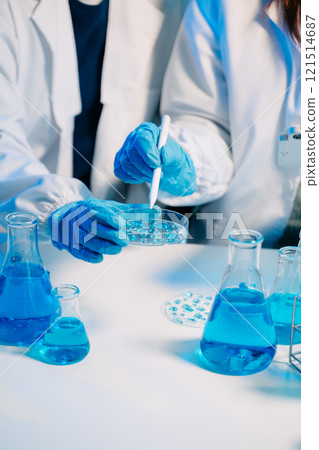 scientists in lab coats conducting research, handling glassware, and working with chemicals 121514687