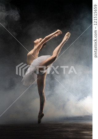 Graceful ballet dancer performing an elegant leap in a misty theater setting 121515659