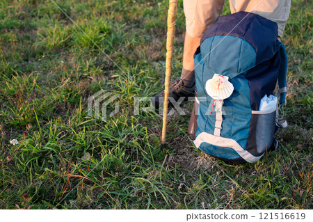 Pilgrim is taking a break during Camino de Santiago, resting his backpack with scallop shell on the grass. Copy space 121516619