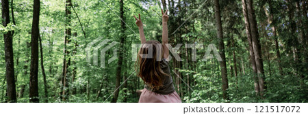 Toddler girl standing in a forest with her arms raised in victorious gesture 121517072