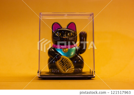 Maneki Neko Japanese lucky cat waving a paw close up on yellow orange background. Chinese symbol of good luck. Welcoming kitty souvenir. Success toy. Maneki Neko Japanese lucky cat waving a paw close up on yellow orange background. Chinese symbol of good luck. Welcoming kitty souvenir. Success toy. 121517963