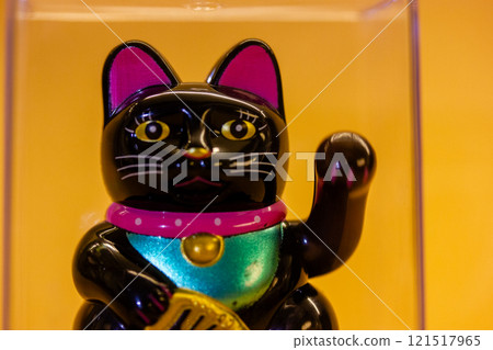 Maneki Neko Japanese lucky cat waving a paw close up on yellow orange background. Chinese symbol of good luck. Welcoming kitty souvenir. Success toy. 121517965