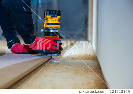 Person Using Yellow Router on Wood Surface with Red Gloves Indoors 121518569