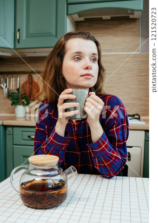 cheerful woman enjoying cup of coffee or tea. lovely lady is sitting at kitchen table and smiling 121520723