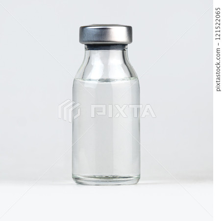Simple glass vial with a metal cap filled with a clear liquid, placed on a white surface 121522065
