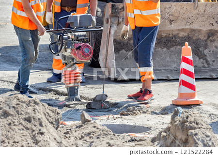 Workers engage in construction activity using a compactor in a busy worksite 121522284
