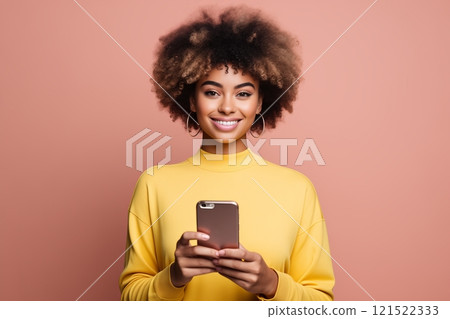 A cheerful woman with curly hair holding a smartphone, dressed in a vibrant yellow sweater against a pink background. A cheerful woman with curly hair holding a smartphone, dressed in a vibrant yellow sweater against a pink background. 121522333