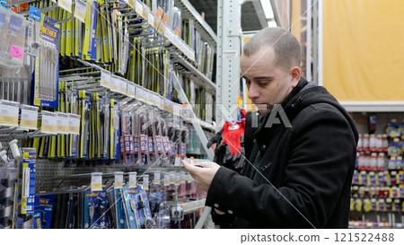Focused male shopper selecting drill bit, comparing options while holding shopping list in hardware store aisle 121522488