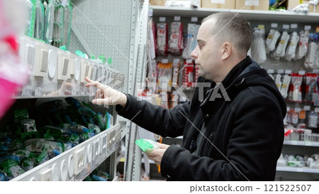 Experienced electrician selecting light switches and electrical components in supply store, comparing options for upcoming technical project 121522507
