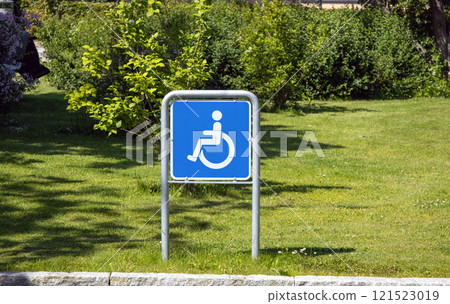 Wheelchair handicap sign in a parking against the backdrop of a green lawn. Wheelchair handicap sign in a parking against the backdrop of a green lawn. 121523019