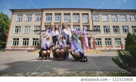 Happy female graduates posing in front of the school building with sashes on their last day of school Happy female graduates posing in front of the school building with sashes on their last day of school 121523908