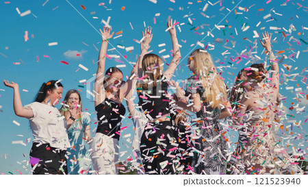 Teenage girls celebrate graduation by tossing colorful confetti into the air against a clear blue sky Teenage girls celebrate graduation by tossing colorful confetti into the air against a clear blue sky 121523940