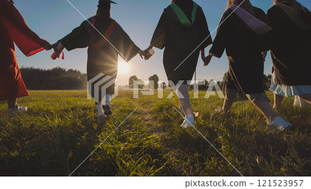 Group of joyful graduates joyfully running through a field at sunset, holding hands and rejoicing in their academic success Group of joyful graduates joyfully running through a field at sunset, holding hands and rejoicing in their academic success 121523957