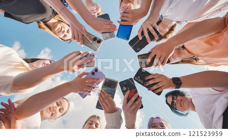 Group of teenagers making circle with smartphones on background of blue sky, taking photo of themselves on their phones, concept of modern communication 121523959
